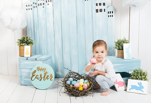 adorable little child sitting in easter decorated room with nest of colorful eggs