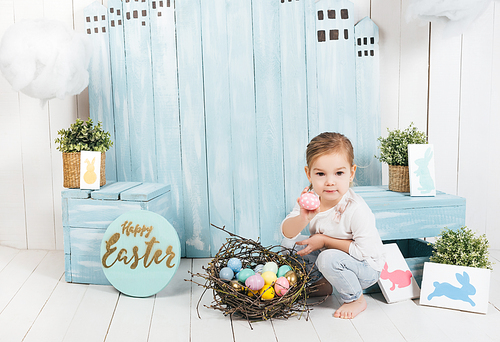 adorable little child sitting in easter decorated room with nest of colorful eggs