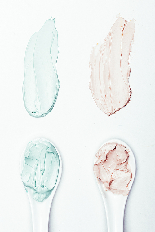 top view of spoons and different clay mask smudges on white surface