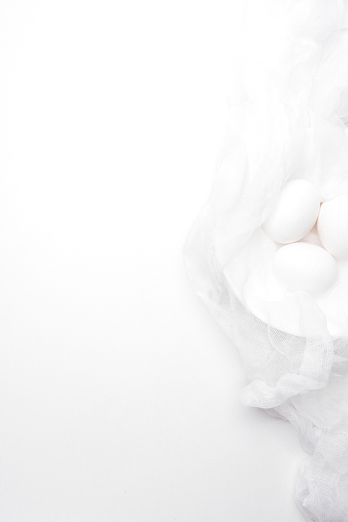 top view of chicken eggs in cheesecloth on white surface