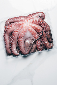 top view of uncooked octopus in plastic container on marble surface