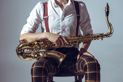 cropped shot of young musician sitting on chair and holding saxophone isolated on grey