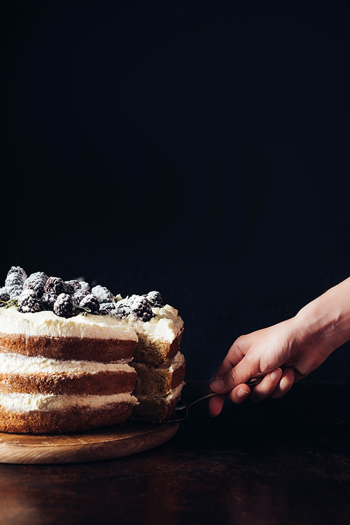 cropped shot of woman serving delicious blackberry cake on black