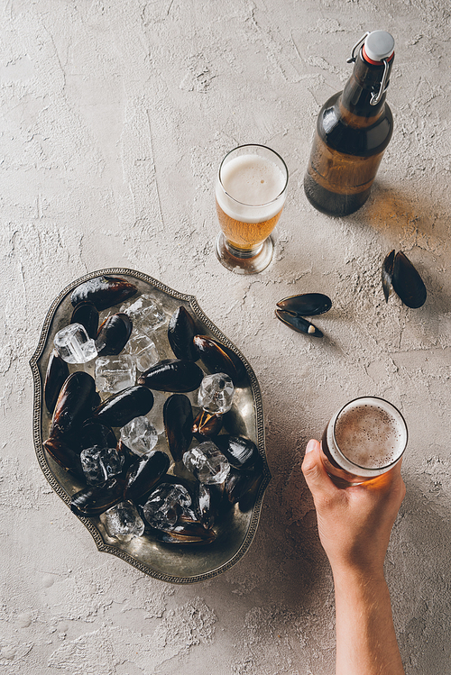 partial view of man with glass of beer and mussels with ice cubes in bowl on tabletop