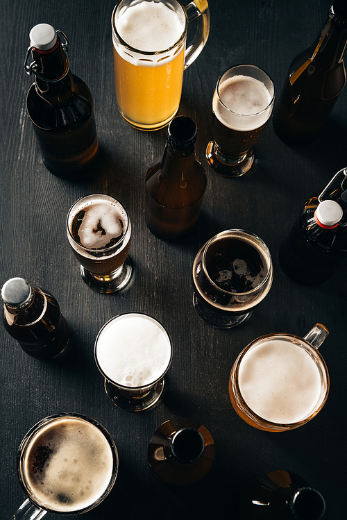 top view of arrangement of bottles and glasses of beer on dark wooden tabletop