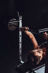 high angle view of female bodybuilder doing exercise with barbell at gym, black background