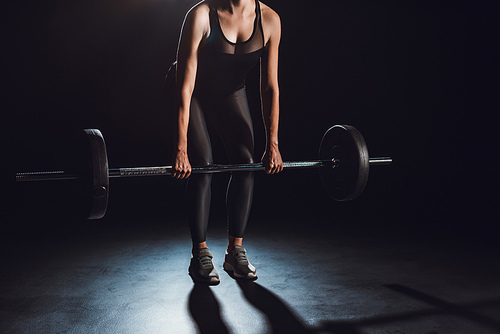 cropped image of female athlete doing exercise with barbell at gym, black background