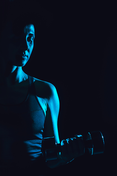 toned picture of female athlete exercising with dumbbell, black background