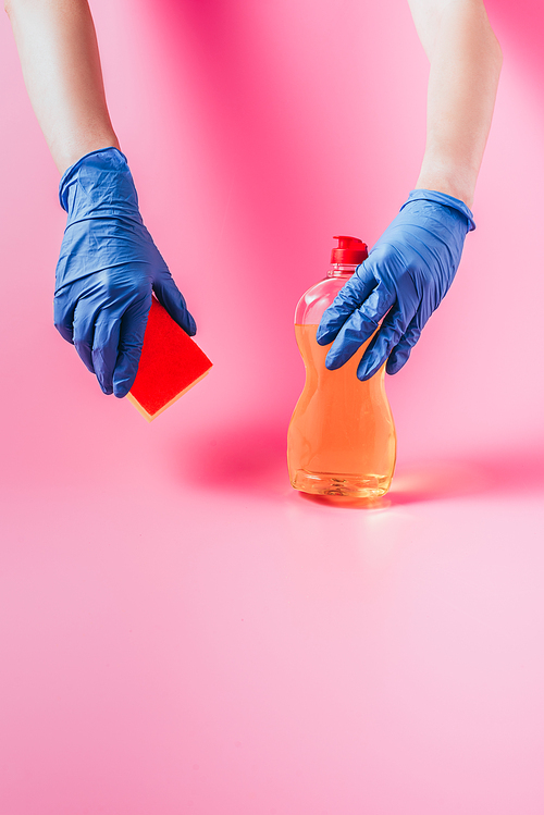 cropped image of woman in rubber glove holding washing sponge and dishwashing liquid, pink background
