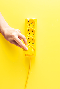 cropped shot of person inserting plug into socket outlet on yellow