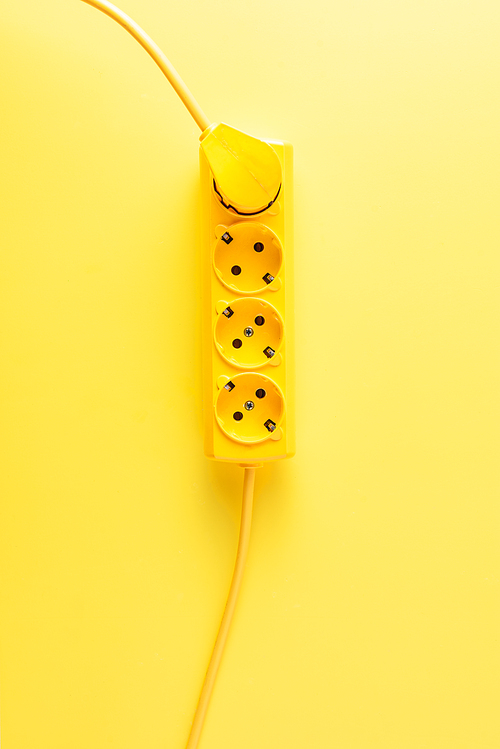 top view of bright yellow socket outlet with plug on yellow background