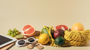 close-up view of sunglasses, earrings, digital tablet and ripe fruits in string bag on brown