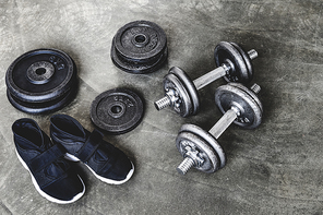 close-up shot of dumbbells with weight plates and sneakers on concrete surface