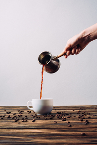 cropped shot of woman pouring coffee into cup from cezve on rustic wooden table