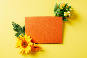 top view of empty orange card, sunflower, gerbera and lily flowers on yellow backdrop