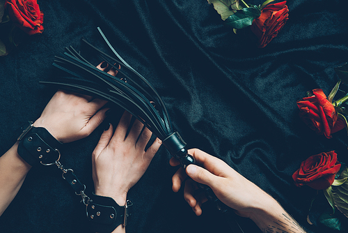 cropped shot of man holding black whip and woman in leather handcuffs