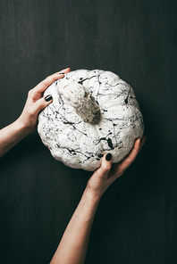 cropped view of female hands holding white pumpkin with black paint splatters, halloween decoration
