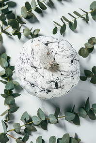 top view of white pumpkin with paint splatters arranged with eucalyptus leaves, halloween decor