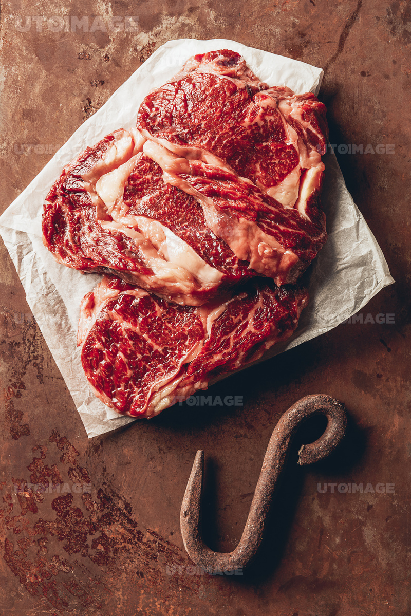 유토이미지 | top view of raw meat steaks and metal hook on brown surface in kitchen