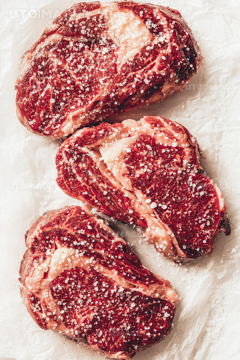 유토이미지 | top view of three pieces of raw meat steaks with salt on baking paper in kitchen