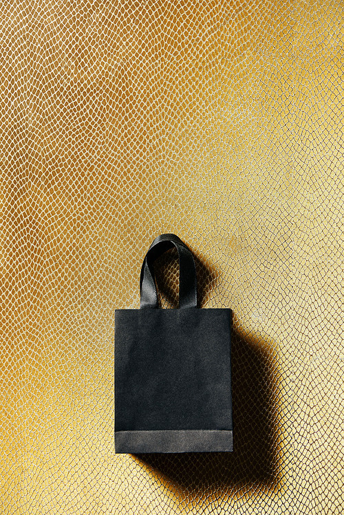 top view of black shopping bag on golden background, black friday concept