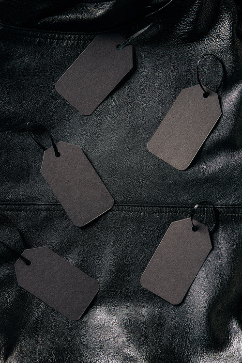 top view of arranged blank price tags on black leather jacket background, black friday concept
