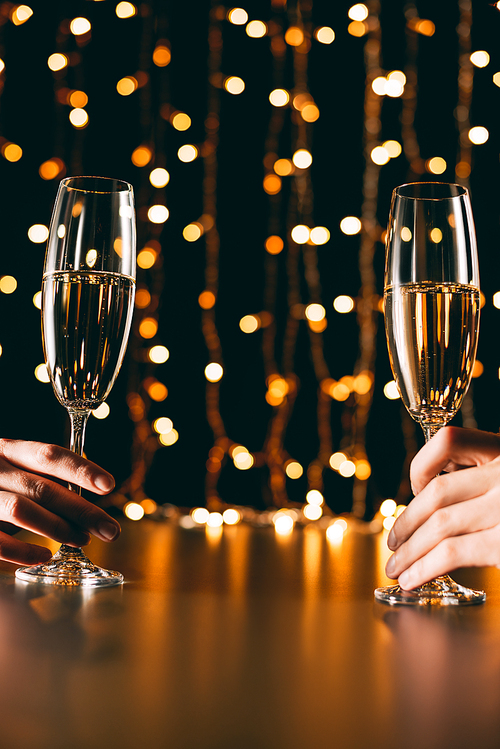 cropped image of couple holding champagne glasses on garland light background, christmas concept