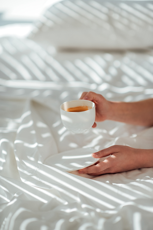 partial view of woman with cup of coffee in bed in morning