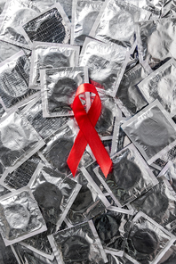 top view of aids awareness red ribbon on silver condoms