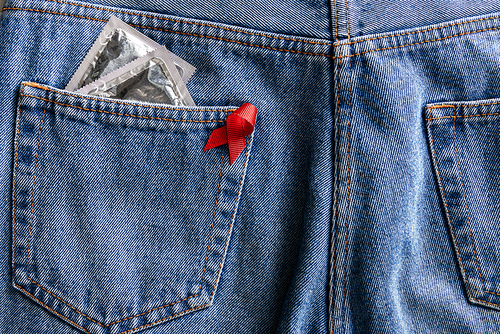 aids awareness red ribbon and silver condoms in pocket of blue jeans