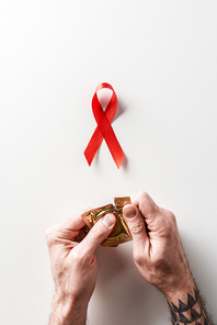 male hands opening golden packaging of condom with aids awareness red ribbon on white background