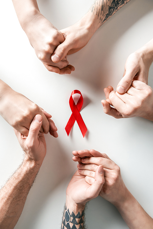 top view of people holding hands and aids awareness red ribbon on white background