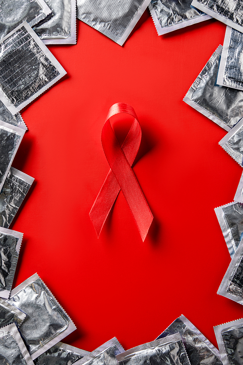 top view of aids awareness red ribbon and silver condoms on red background
