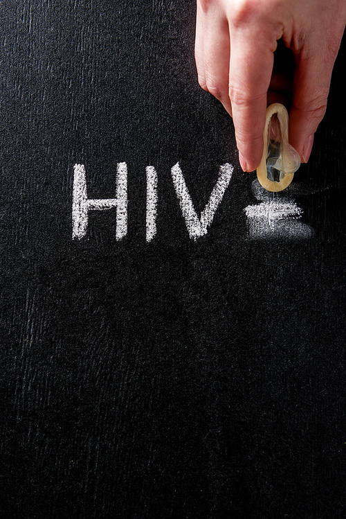 top view female hand holding condom with hiv sign on black background