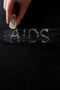 top view female hand holding condom with aids sign on black background