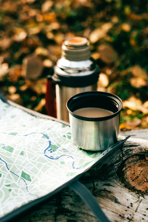 coffee in metallic thermos cup on travel map on blurred autumnal background