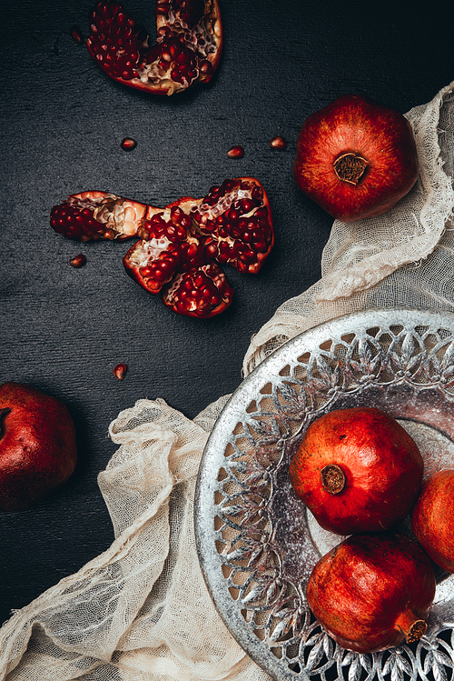 food composition with ripe and fresh pomegranates, metal bowl and gauze on black tabletop