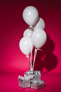 bundle of white balloons and silver gift boxes on burgundy