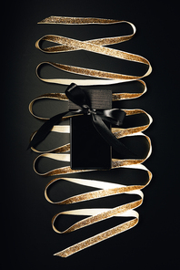 black perfume bottle with bow and shiny golden ribbon on black
