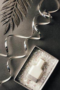 perfume bottle in box, silver ribbons and shiny decorative leaves on grey