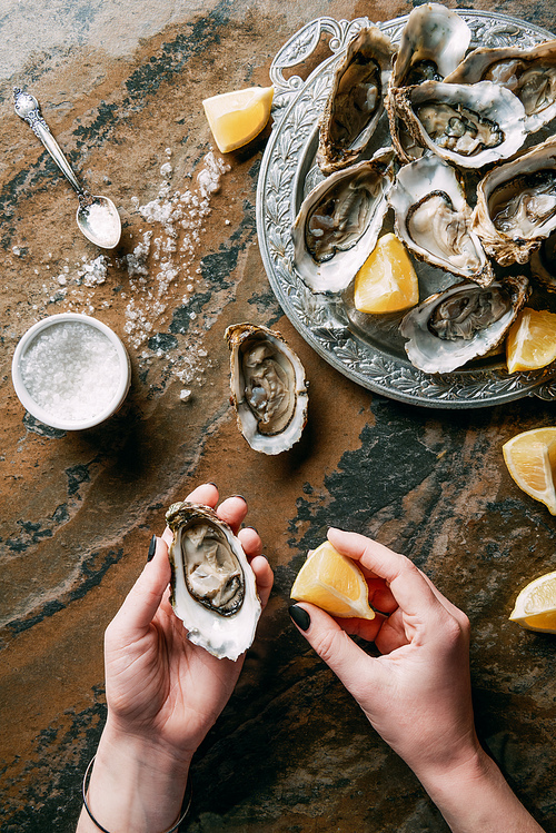 cropped shot of woman holding oyster and lemon piece in hand at grungy tabletop