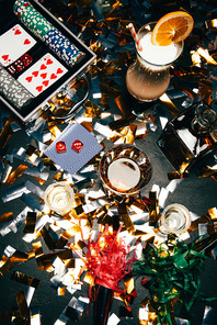 elevated view of alcoholic cocktails, playing cards, poker chips and party horns on table covered by golden confetti