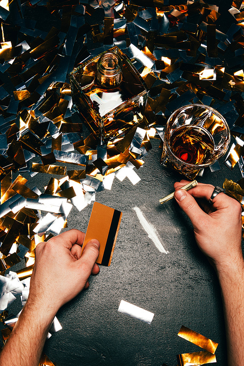 partial view of man with rolled banknote and credit card going to sniff cocaine at table covered by golden confetti