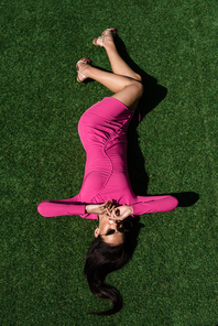 top view of attractive woman in dress and sunglasses posing and lying on grass outside