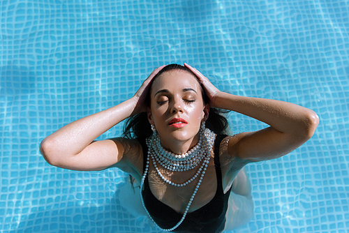 top view of attractive woman in black swimsuit and pearl necklace posing in pool
