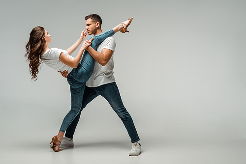 dancers in t-shirts and jeans dancing bachata on grey background