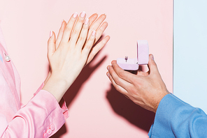 cropped view of man doing marriage proposal to clapping woman on pink and blue background