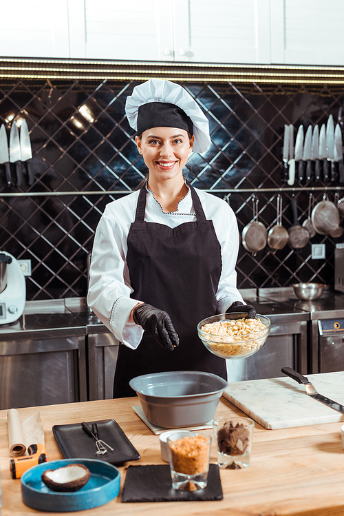 cheerful chocolatier in apron adding white chocolate chips into bowl