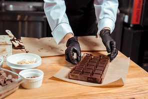 cropped view of chocolatier holding chocolate molds with chocolate near baking paper