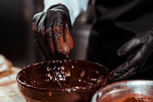 cropped view of chocolatier in black latex glove holding chocolate ball near bowl with melted chocolate